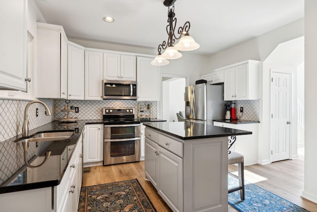 kitchen featuring stainless steel appliances, a breakfast bar, a sink, white cabinets, and dark countertops