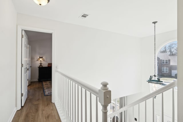 hall featuring an upstairs landing, visible vents, baseboards, and wood finished floors