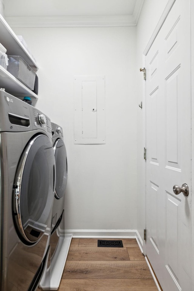 laundry area featuring crown molding, washing machine and dryer, wood finished floors, laundry area, and electric panel