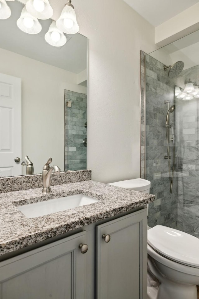 full bathroom with toilet, tiled shower, and vanity