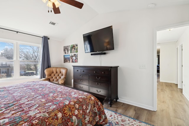 bedroom featuring ceiling fan, wood finished floors, visible vents, baseboards, and vaulted ceiling