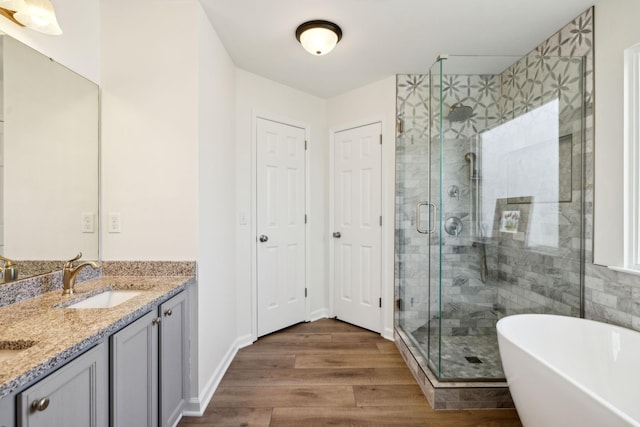 full bathroom with a stall shower, double vanity, a freestanding tub, and wood finished floors