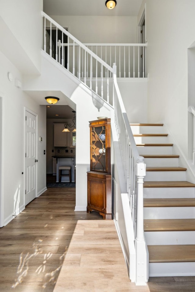 stairs featuring a towering ceiling, baseboards, and wood finished floors