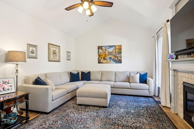 living room with vaulted ceiling, a tiled fireplace, wood finished floors, and a ceiling fan