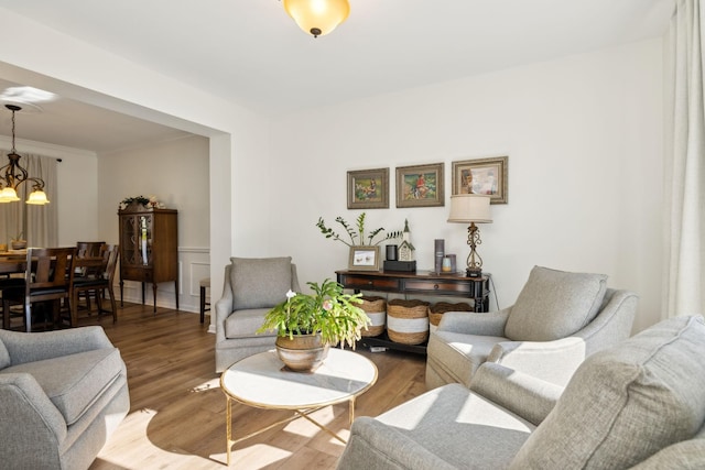 living area with an inviting chandelier, ornamental molding, wood finished floors, and wainscoting