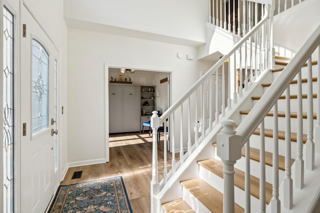 entrance foyer featuring stairs, a high ceiling, wood finished floors, and visible vents