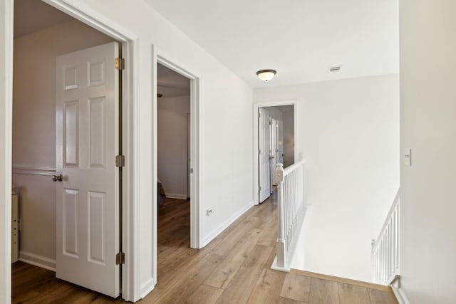 hall featuring visible vents, light wood-type flooring, an upstairs landing, and baseboards