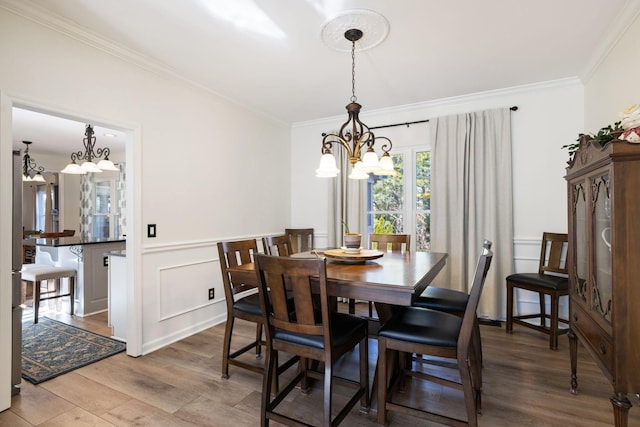 dining space featuring a wainscoted wall, a notable chandelier, a decorative wall, ornamental molding, and wood finished floors