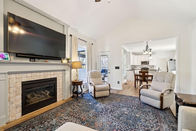 living area with vaulted ceiling, a fireplace, wood finished floors, and baseboards