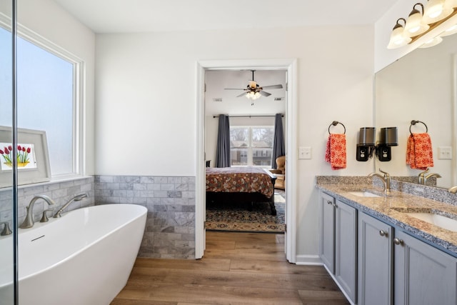 full bathroom with double vanity, connected bathroom, wood finished floors, a freestanding bath, and a sink