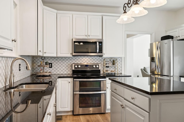 kitchen with stainless steel appliances, dark countertops, decorative backsplash, white cabinets, and a sink