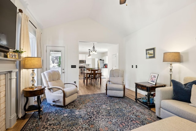 living room with ceiling fan, wood finished floors, baseboards, vaulted ceiling, and a brick fireplace