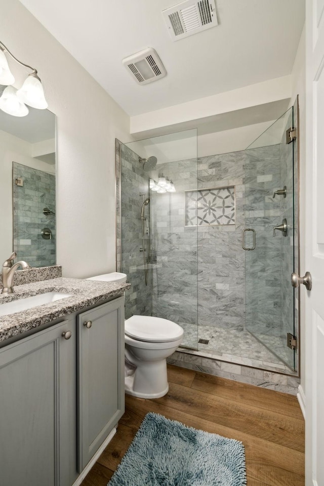 full bath with a stall shower, visible vents, vanity, and wood finished floors