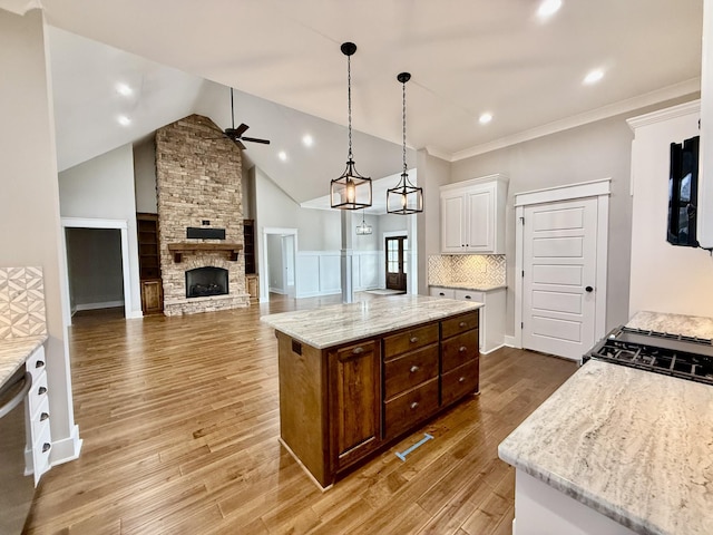 kitchen with a ceiling fan, white cabinetry, a stone fireplace, and light wood finished floors