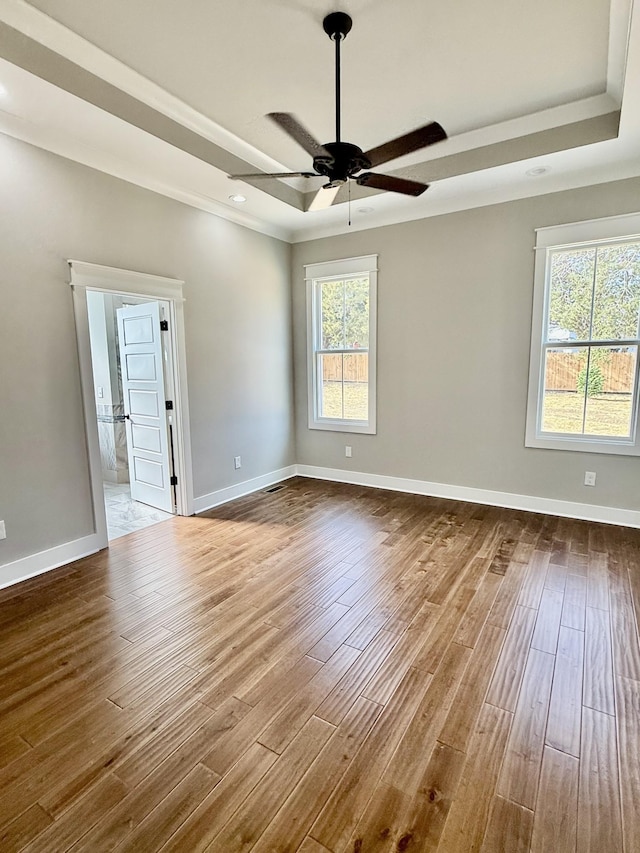 empty room with wood finished floors, a raised ceiling, a ceiling fan, and baseboards