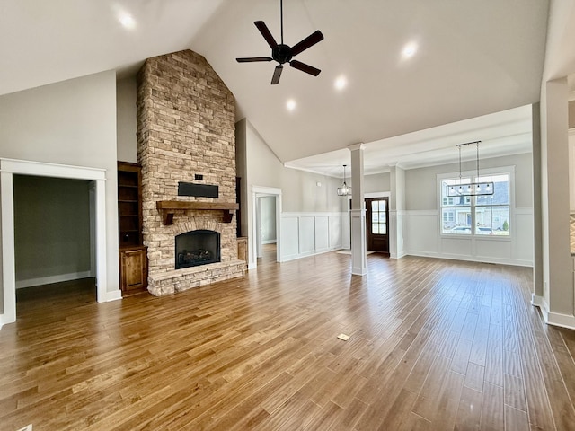 unfurnished living room with a wainscoted wall, a ceiling fan, a stone fireplace, wood finished floors, and high vaulted ceiling