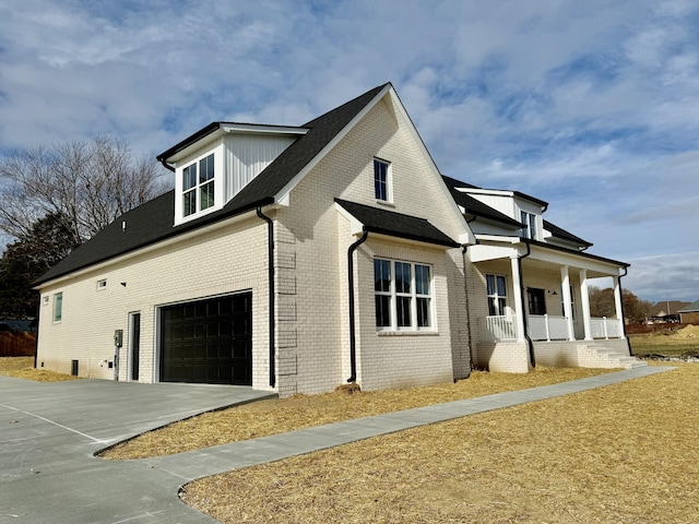 view of side of home featuring a porch, brick siding, and concrete driveway