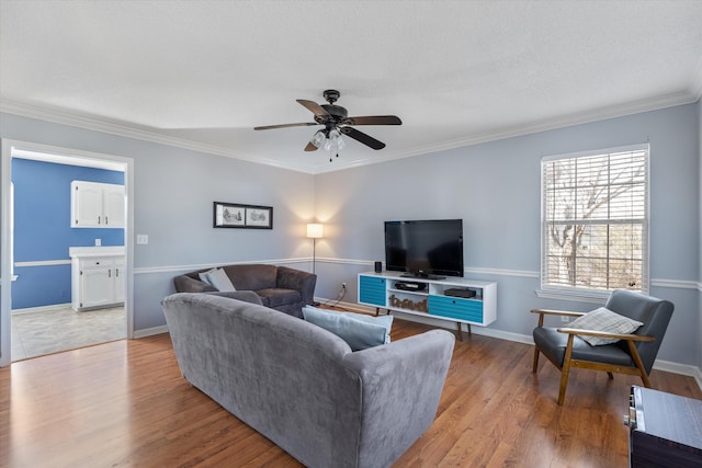 living area with ornamental molding, a ceiling fan, baseboards, and wood finished floors