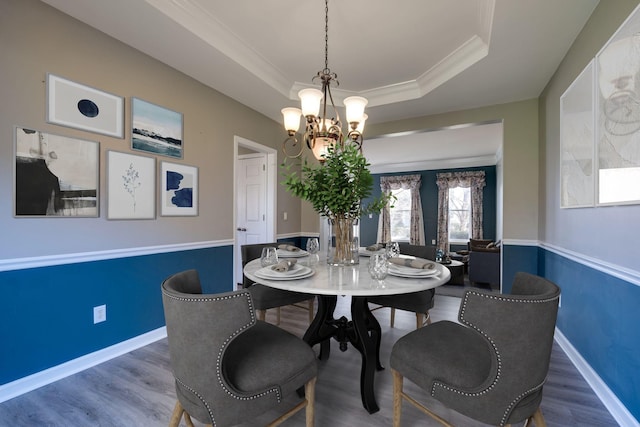 dining area with a notable chandelier, crown molding, a raised ceiling, wood finished floors, and baseboards