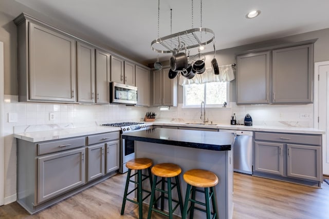 kitchen featuring a breakfast bar, gray cabinets, stainless steel appliances, and a sink