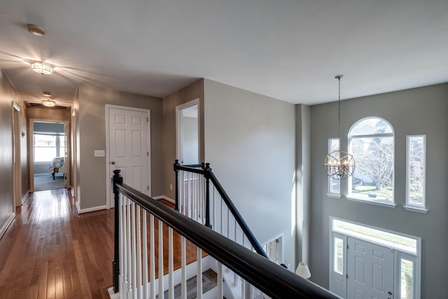 hall with dark wood-type flooring, a chandelier, baseboards, and an upstairs landing