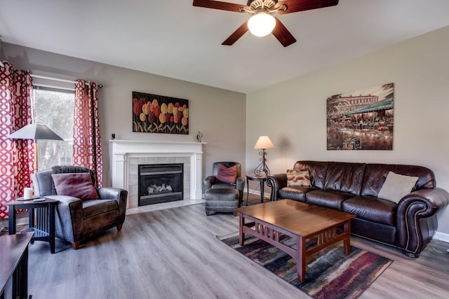 living area featuring a tile fireplace, wood finished floors, a ceiling fan, and baseboards