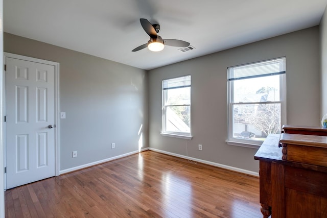 spare room with a ceiling fan, wood-type flooring, visible vents, and baseboards