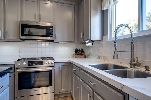 kitchen with appliances with stainless steel finishes, backsplash, a sink, and gray cabinetry