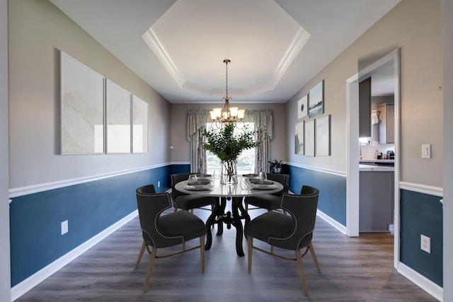 dining area with dark wood-type flooring, a raised ceiling, crown molding, and a notable chandelier