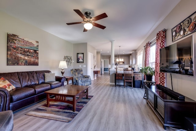 living room with ceiling fan with notable chandelier, decorative columns, and light wood-style flooring