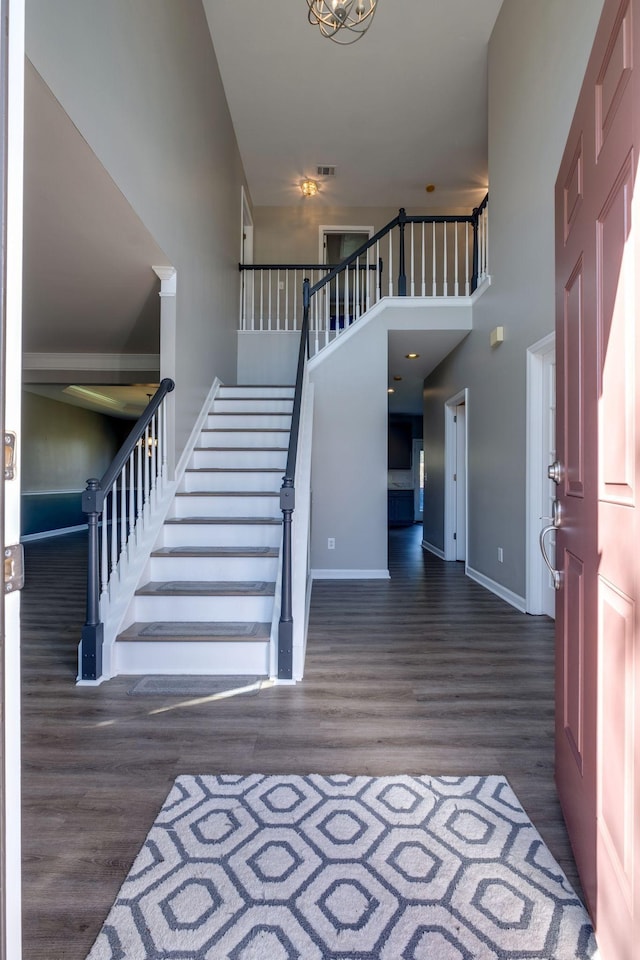 staircase featuring a high ceiling, visible vents, baseboards, and wood finished floors