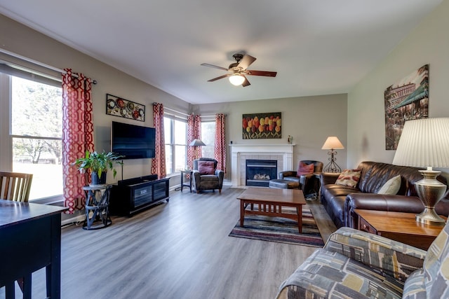 living area with a tile fireplace, wood finished floors, and a ceiling fan