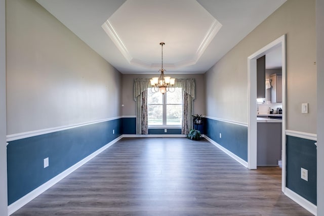 unfurnished dining area featuring a tray ceiling, dark wood finished floors, crown molding, and a chandelier