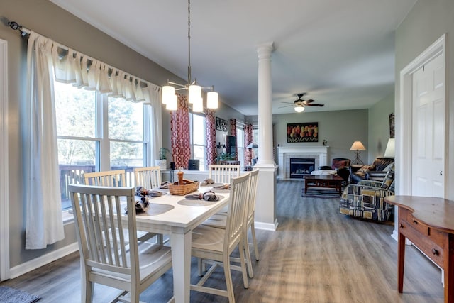 dining space with a ceiling fan, a fireplace, ornate columns, and wood finished floors