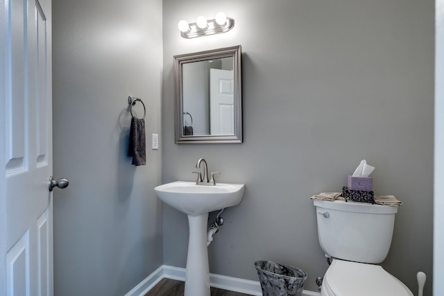 half bath with toilet, baseboards, and wood finished floors