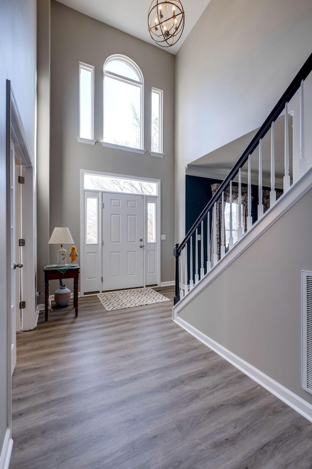 foyer featuring a chandelier, wood finished floors, a towering ceiling, baseboards, and stairway