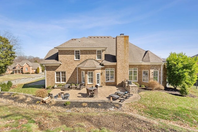 rear view of property featuring a patio area, a lawn, a chimney, and brick siding