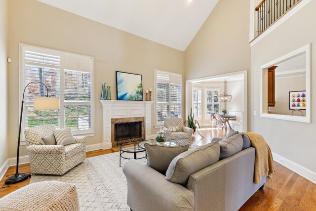 living area with baseboards, a premium fireplace, wood finished floors, high vaulted ceiling, and a notable chandelier