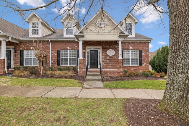 view of front of property with a shingled roof, a front lawn, and brick siding