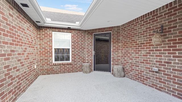 entrance to property with a shingled roof and brick siding