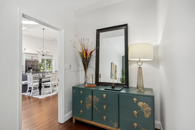 hall featuring dark wood-type flooring, baseboards, and an inviting chandelier