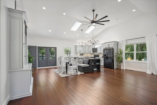 living area with high vaulted ceiling, recessed lighting, ceiling fan with notable chandelier, a skylight, and dark wood finished floors