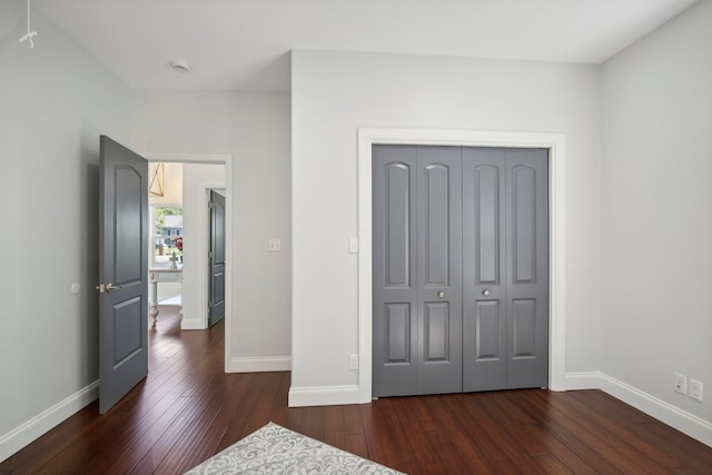 unfurnished bedroom featuring baseboards, dark wood finished floors, and a closet