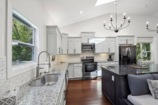 kitchen featuring stainless steel appliances, a sink, light stone countertops, dark wood-style floors, and pendant lighting