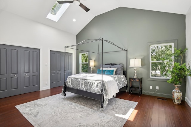 bedroom with high vaulted ceiling, a skylight, wood finished floors, visible vents, and multiple closets