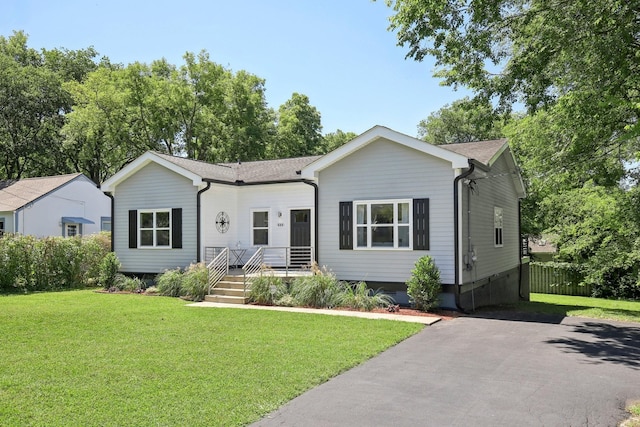 ranch-style house featuring driveway, roof with shingles, a front yard, and fence