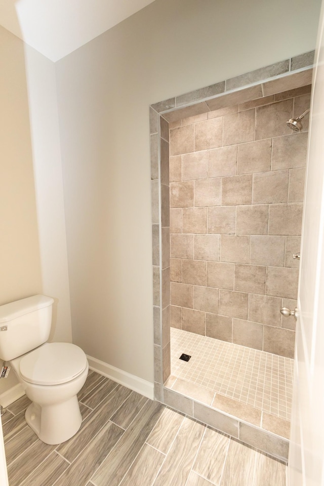 bathroom featuring wood finish floors, baseboards, a tile shower, and toilet