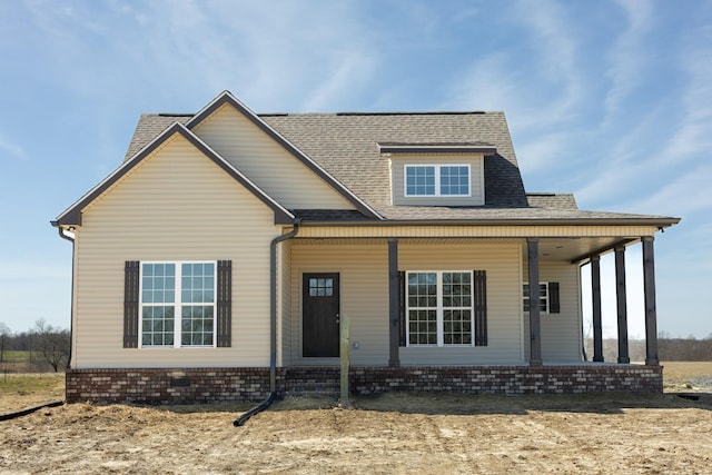 view of front of home with a porch, roof with shingles, and brick siding