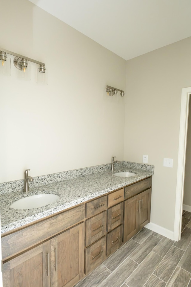 full bathroom featuring double vanity, wood tiled floor, baseboards, and a sink