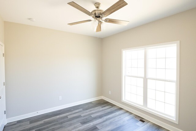 empty room featuring a ceiling fan, dark wood finished floors, visible vents, and baseboards